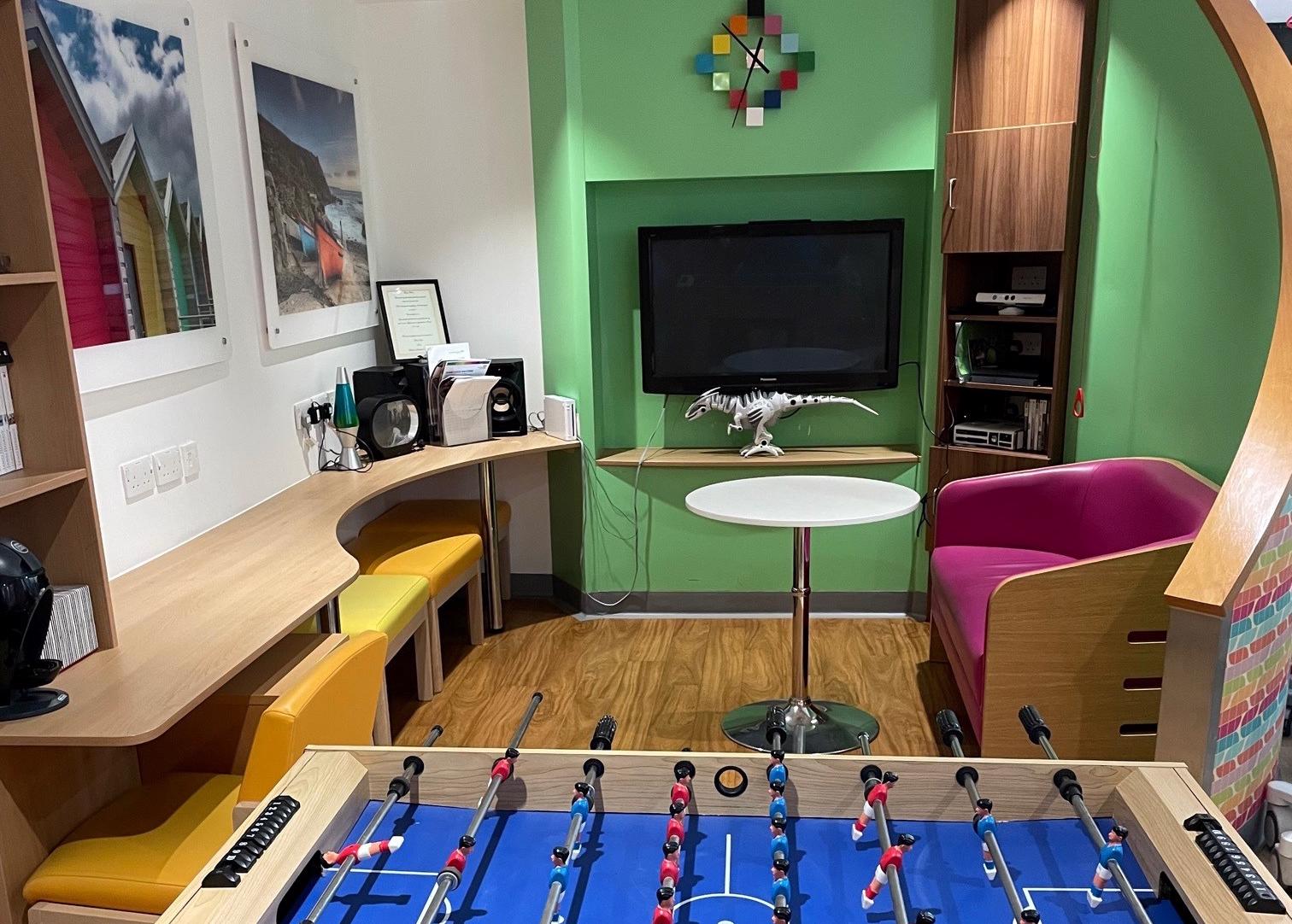 Inside ward E2 showing table football, seating areas, a television screen and dinosaur model.