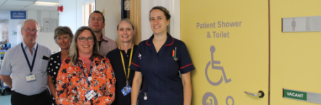 Team photo of staff, beside a yellow door for a patient shower and toilet.